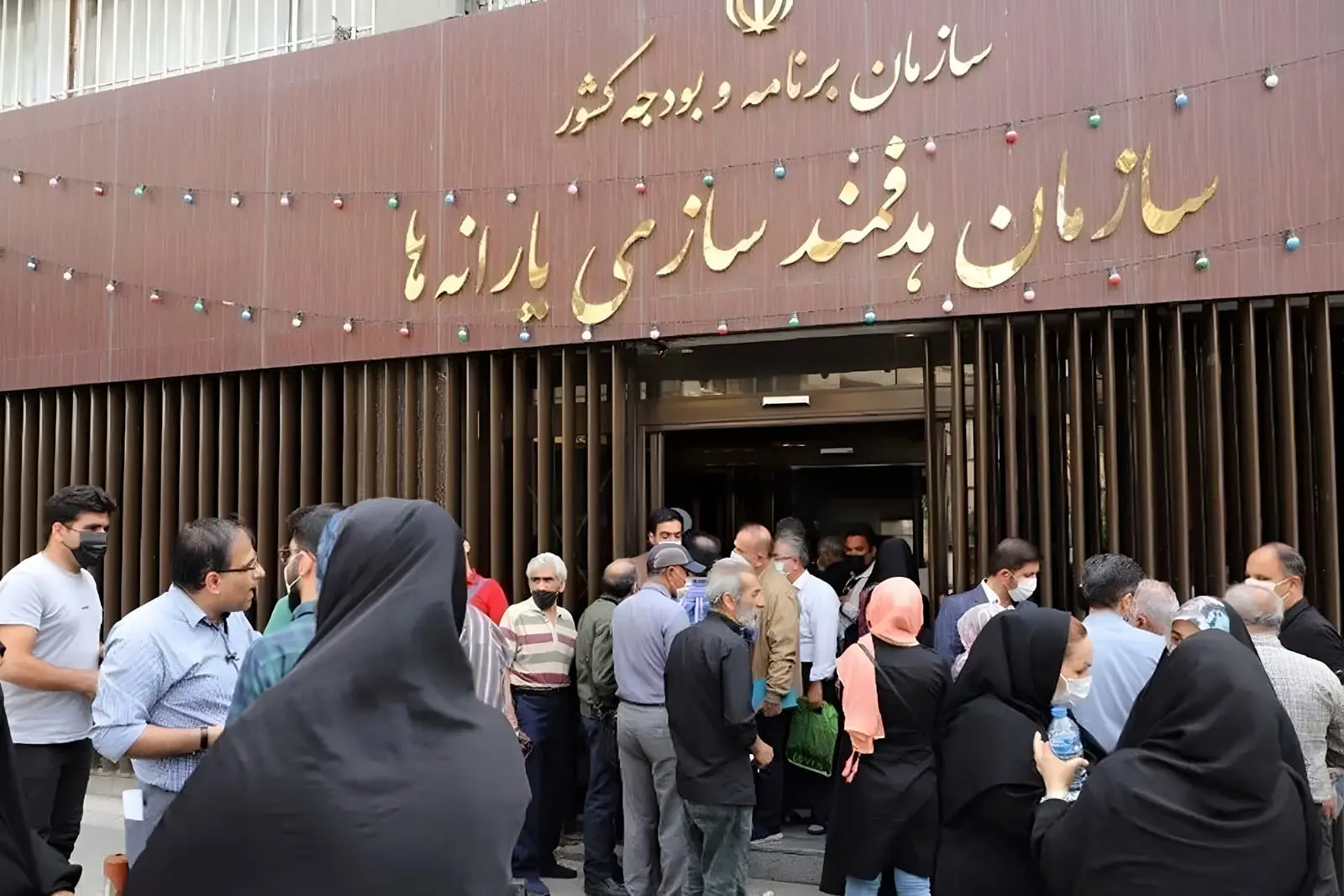 مجموعه‌ای از افراد در صف انتظار مقابل ساختمان سازمان هدفمندسازی یارانه‌ها