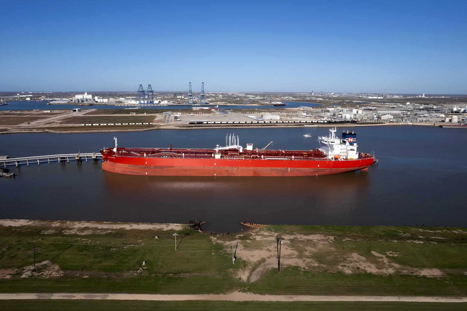 کشتی سوپرتانکر (Supertanker) قرمز رنگ در حال حرکت در آب‌های بندر صنعتی