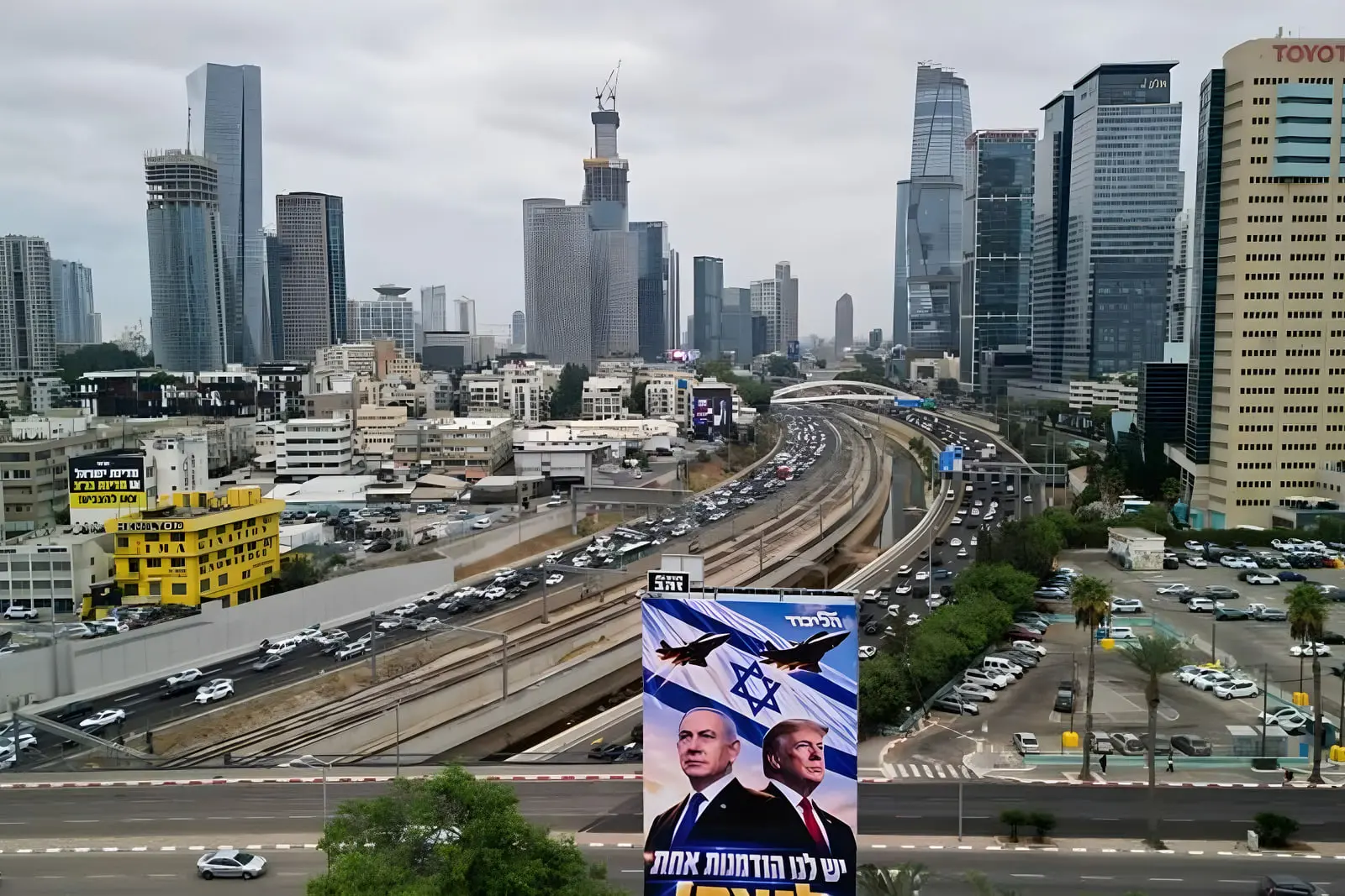 بزرگراه پرتردد در میان آسمان‌خراش‌های شهر تل‌آویو (Tel Aviv) با بیلبورد تبلیغاتی در جلو