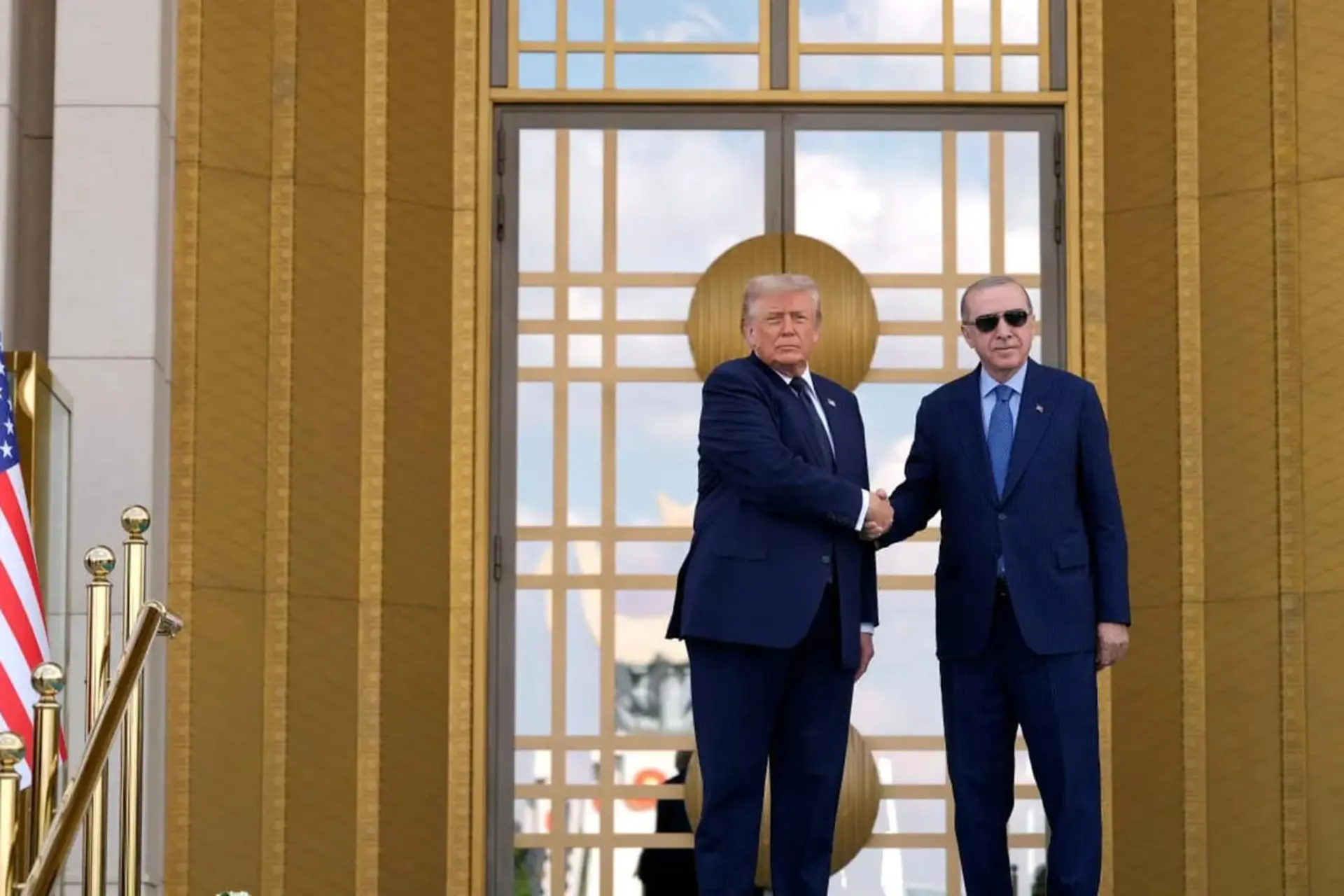 دونالد ترامپ و رجب طیب اردوغان در مقابل یک ساختمان با درهای طلایی با هم دست می‌دهند.