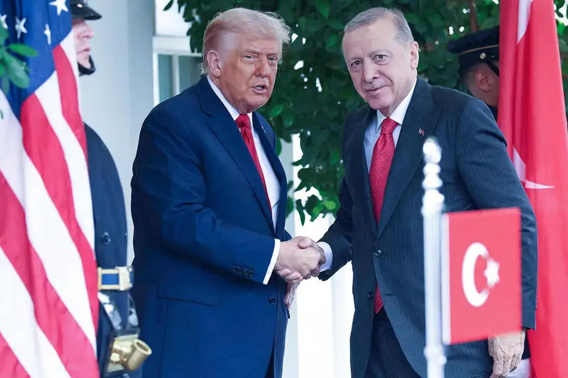 دونالد ترامپ و رجب طیب اردوغان در حال دست دادن در یک مراسم رسمی در کنار پرچم‌های آمریکا و ترکیه هستند.