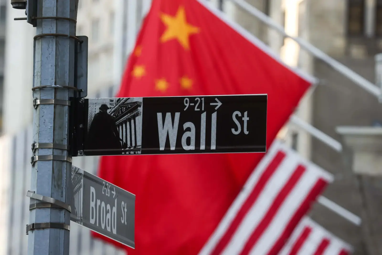 تابلوی خیابان وال استریت (Wall St) در مقابل پرچم‌های چین و آمریکا