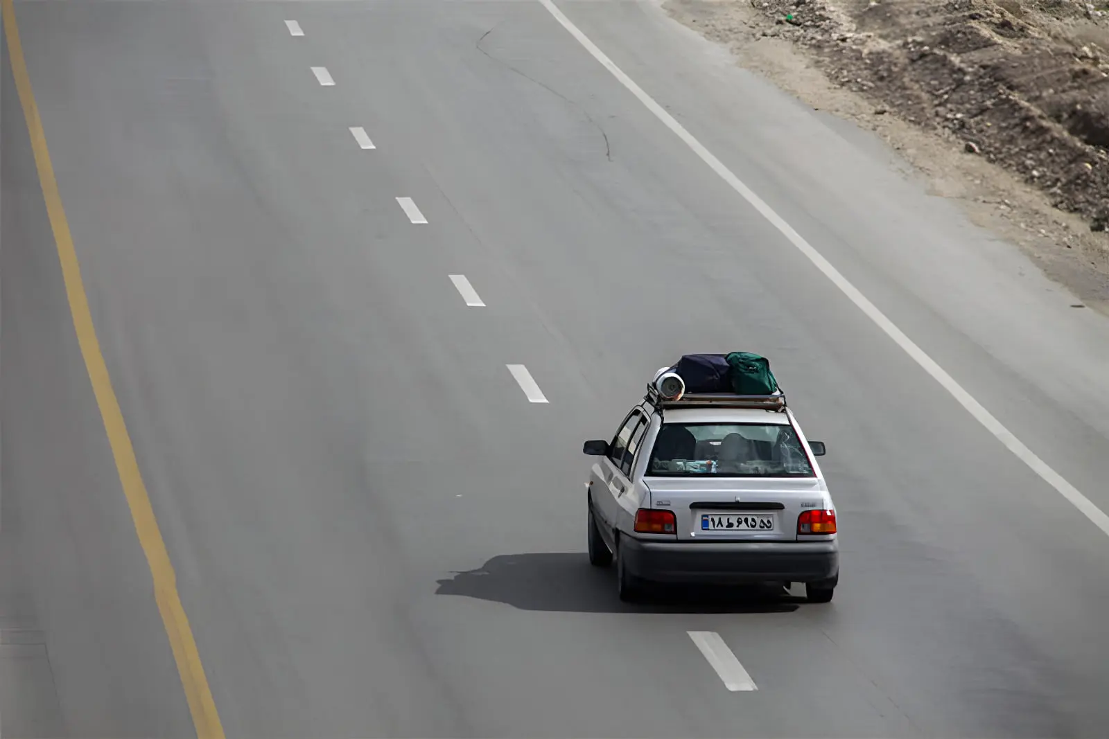 خودروی سفید حامل بار مسافرتی در حال حرکت در جاده