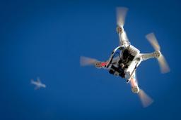 پهپاد کوادکوپتر (Quadcopter) سفید رنگ در حال پرواز در آسمان آبی