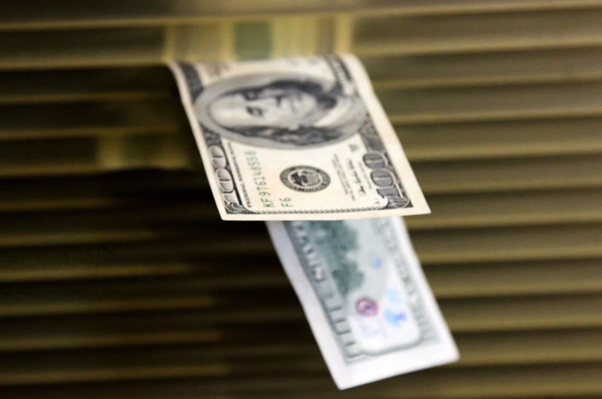 اسکناس ۱۰۰ دلاری آمریکا در پس‌زمینه‌ای تار