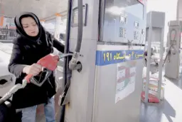 یک زن در حال استفاده از نازل پمپ بنزین برای سوخت زدن خودرو است.