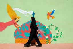 زن با پوشش سیاه در حال عبور از مقابل نقاشی دیواری رنگی