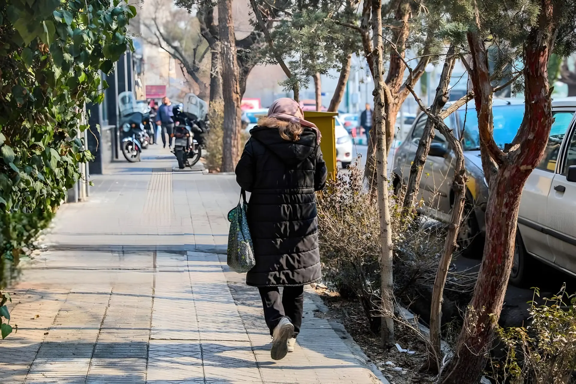 زن با پوشش زمستانی در حال حرکت در پیاده‌روی کنار خیابان