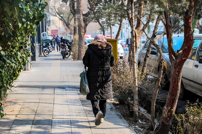 زن با پوشش زمستانی در حال حرکت در پیاده‌روی کنار خیابان